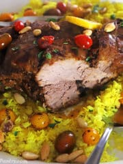 A close look at a leg of lamb with a piece carved out on a yellow rice platter.