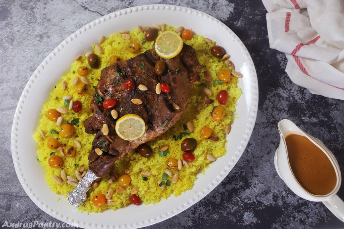 A big white serving platter with roasted leg of lamb and yellow rice garnished with roasted nuts.