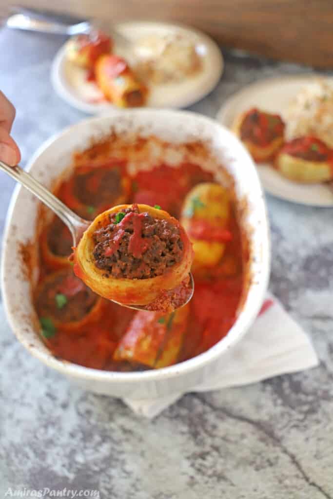 A hand holding a spoon with an artichoke stuffed with ground meat.