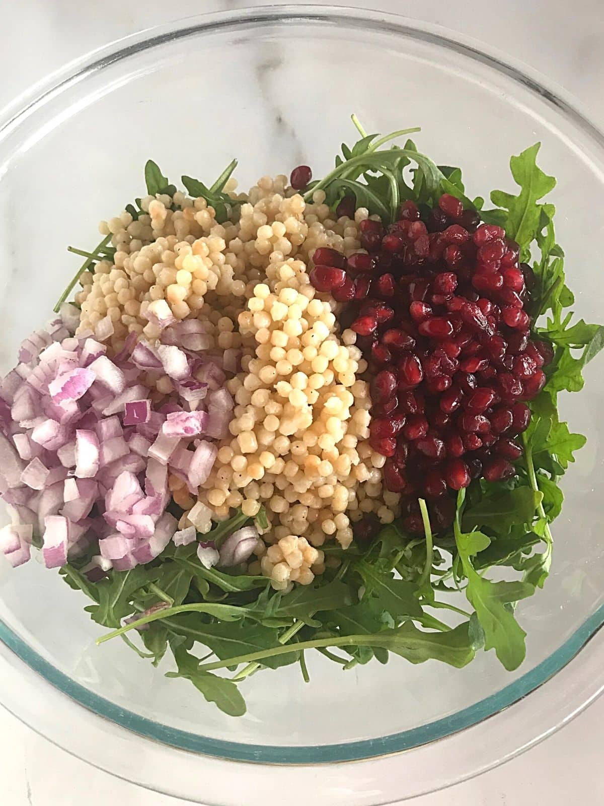 A bowl with mediterranean couscous salad ingredients ready to be mixed.