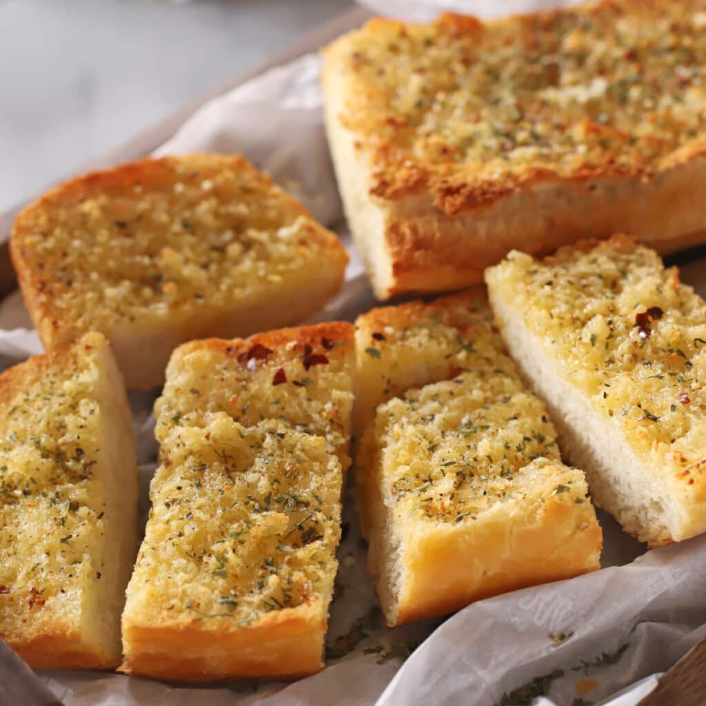 A close up image of garlic bread placed on parchment paper.