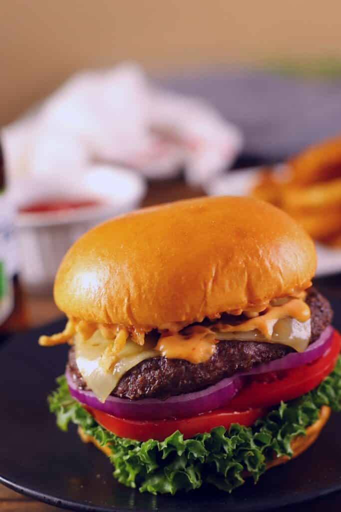 Hamburger sandwich with lettuve, melted cheese, tomatoes and some ketchup on the back.