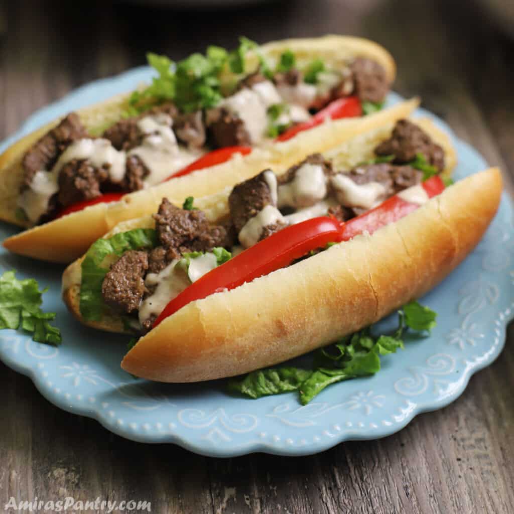 Two liver sandwiches on a blue plate and garnished with lettuce and tahini sauce.