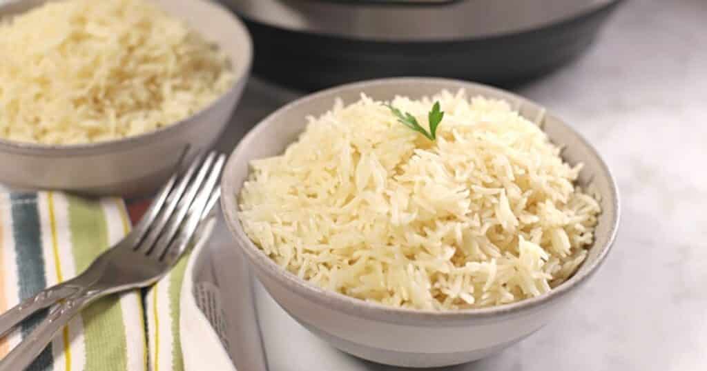 A bowl of basmati rice with forks on the side and an instant pot in the back.