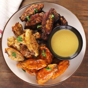 A serving plate of different trypes of air fried wings with a small bowl of sauce on the side.