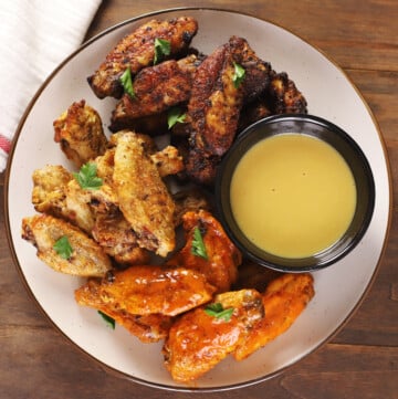 A serving plate of different trypes of air fried wings with a small bowl of sauce on the side.
