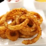 A close up photo of air fried onion rings on a white plate.