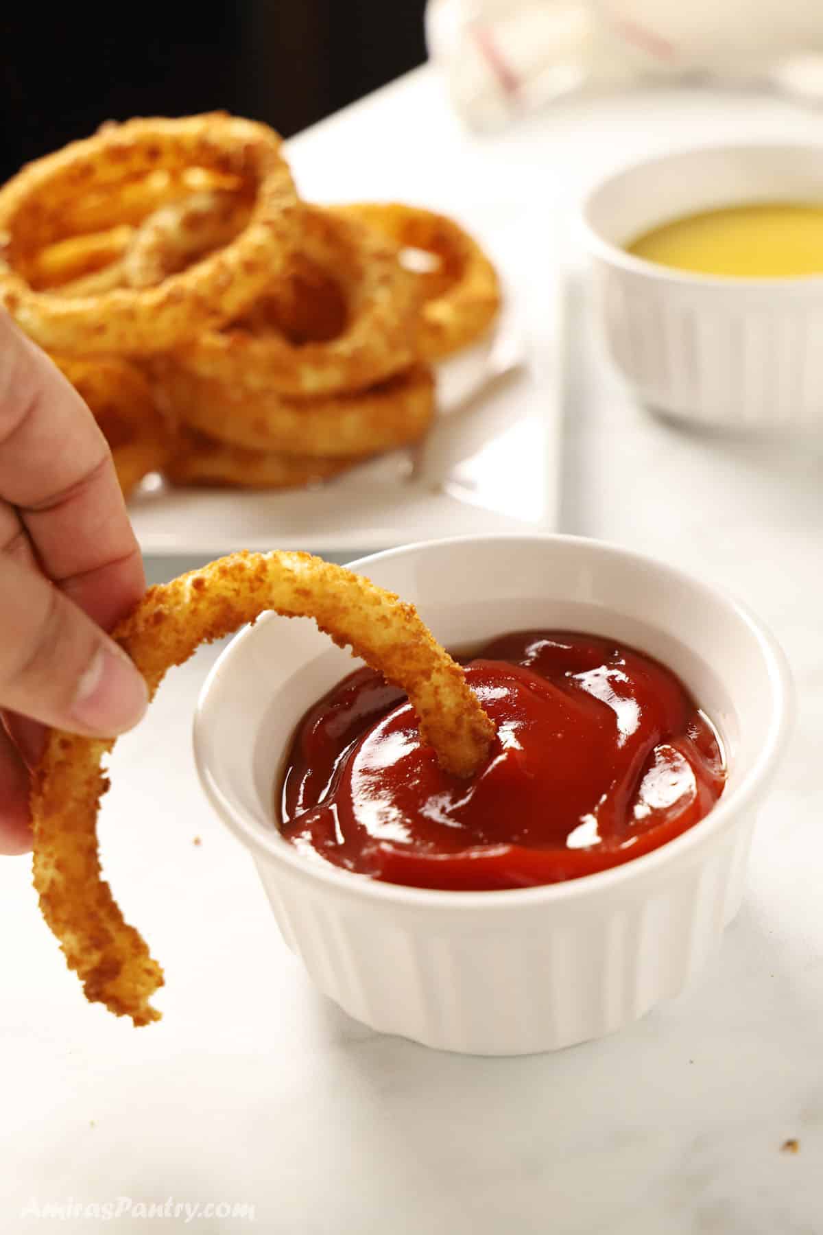 A hand dipping one onion ring in sauce.