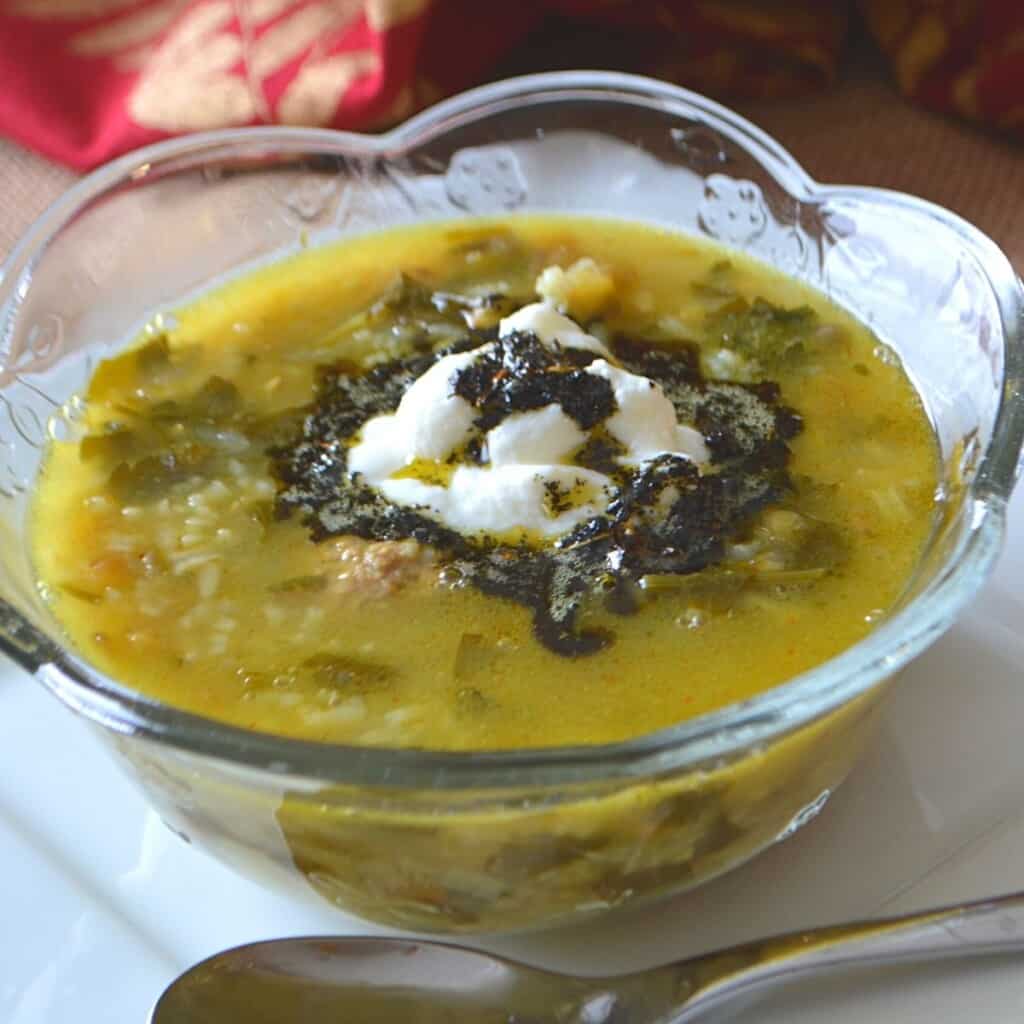 Persian soup in a clear glass bowl with a spoon on the side.