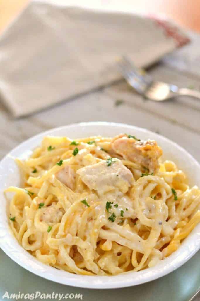 A white plate with some chicken tetrazzini and a fork in the back.
