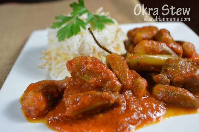 Okra stew in a white plate with rice in the back.