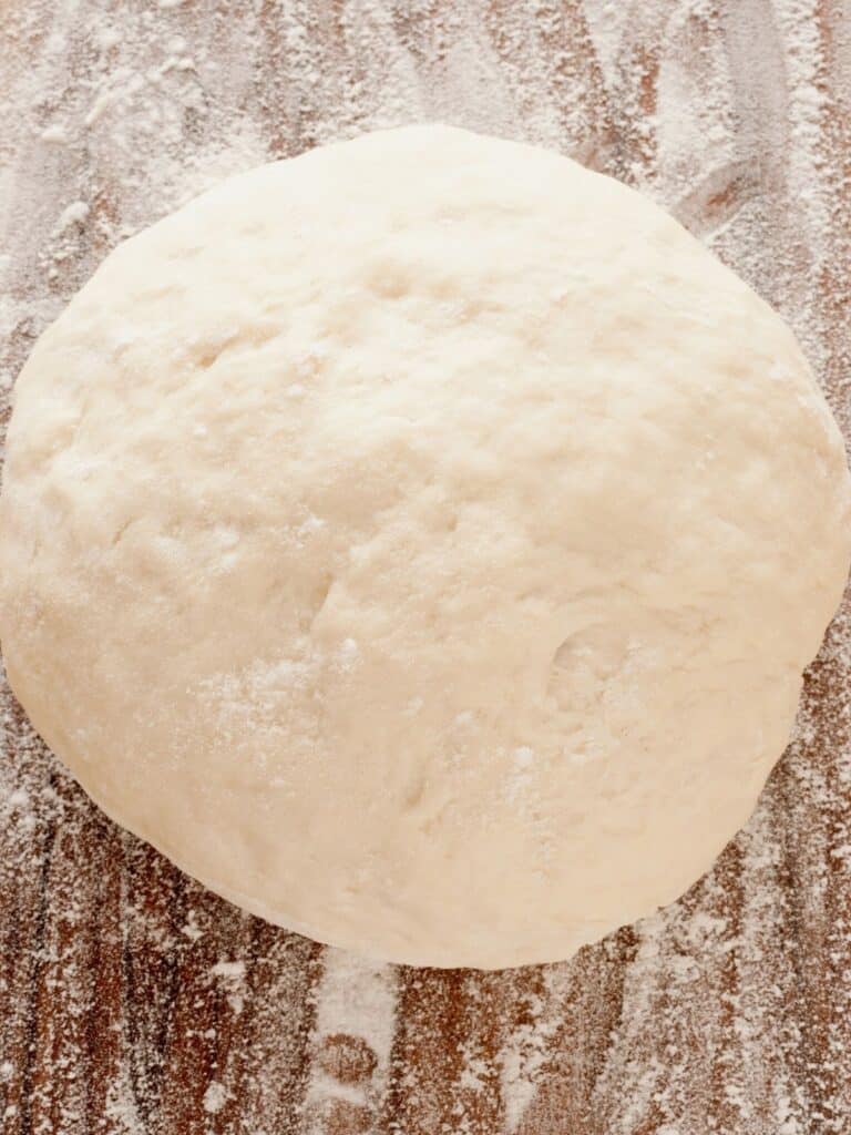 A bird's eye image of a pizza dough placed on a wooden surface.