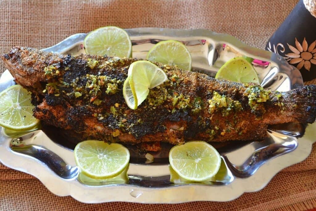 A grilled trout on a silver serving platter with lemon rinds.