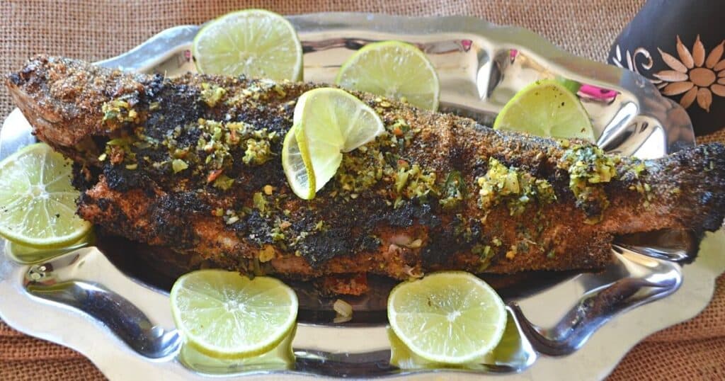 A grilled trout on a silver serving platter with lemon rinds.