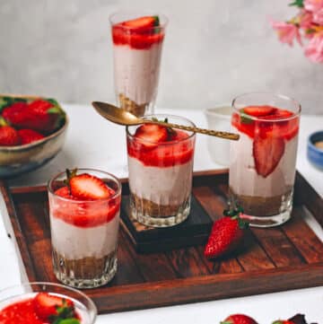 A brown wooden tray with cups filled with strawberry creamcheese and topped with cut strawberries.