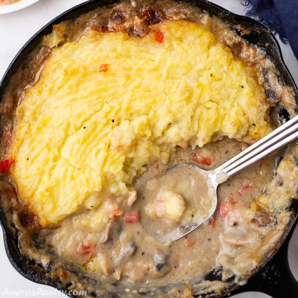 A bird's eye view of a cast iron skillet with chicken and mashed potatoes with a spoon in it.