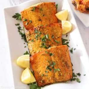 Air fried salmon pieces on a white platter garnished with lemon wedges and parsley.