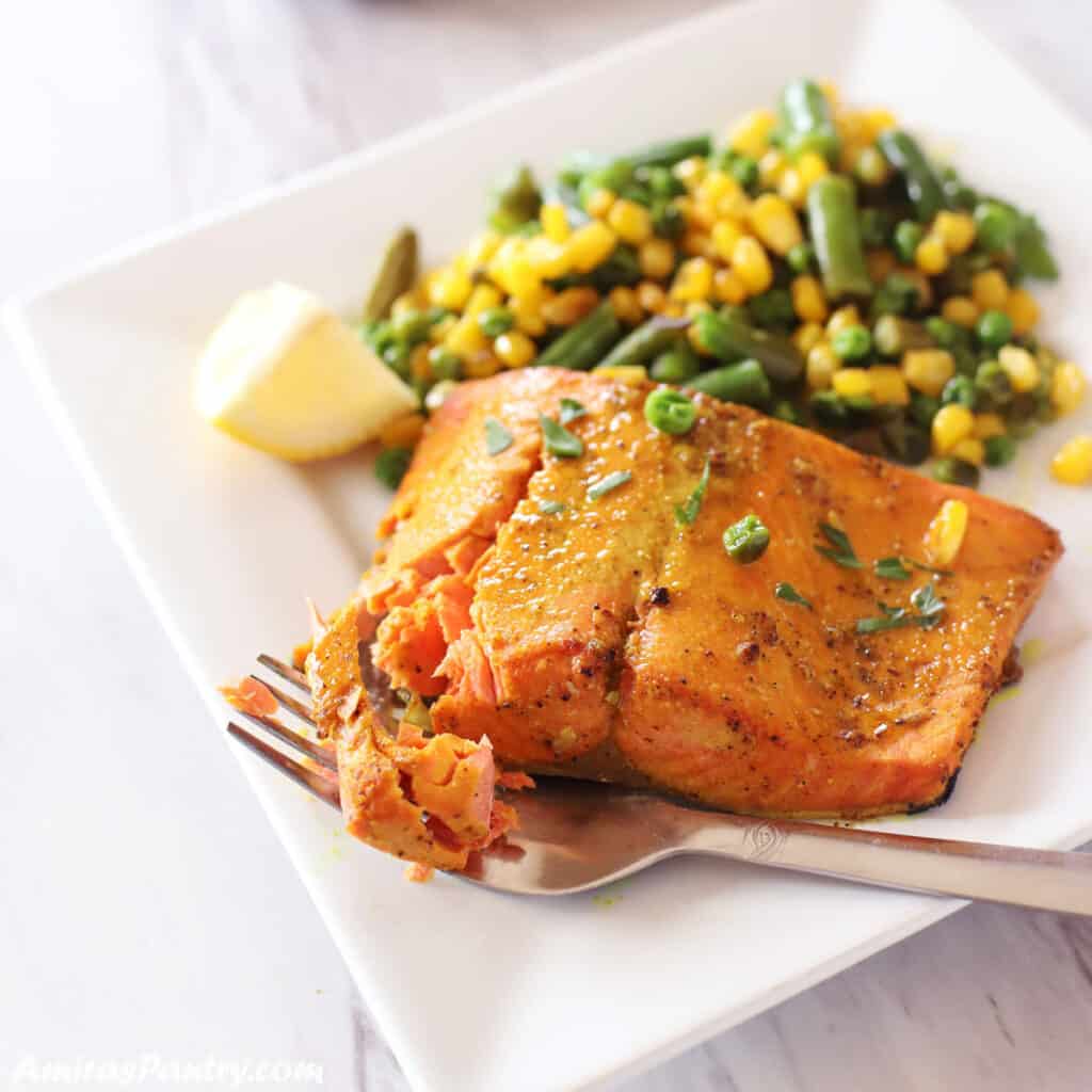 A piece of air fryer salmon placed on a whote plate with sauteed veggies and a fork.