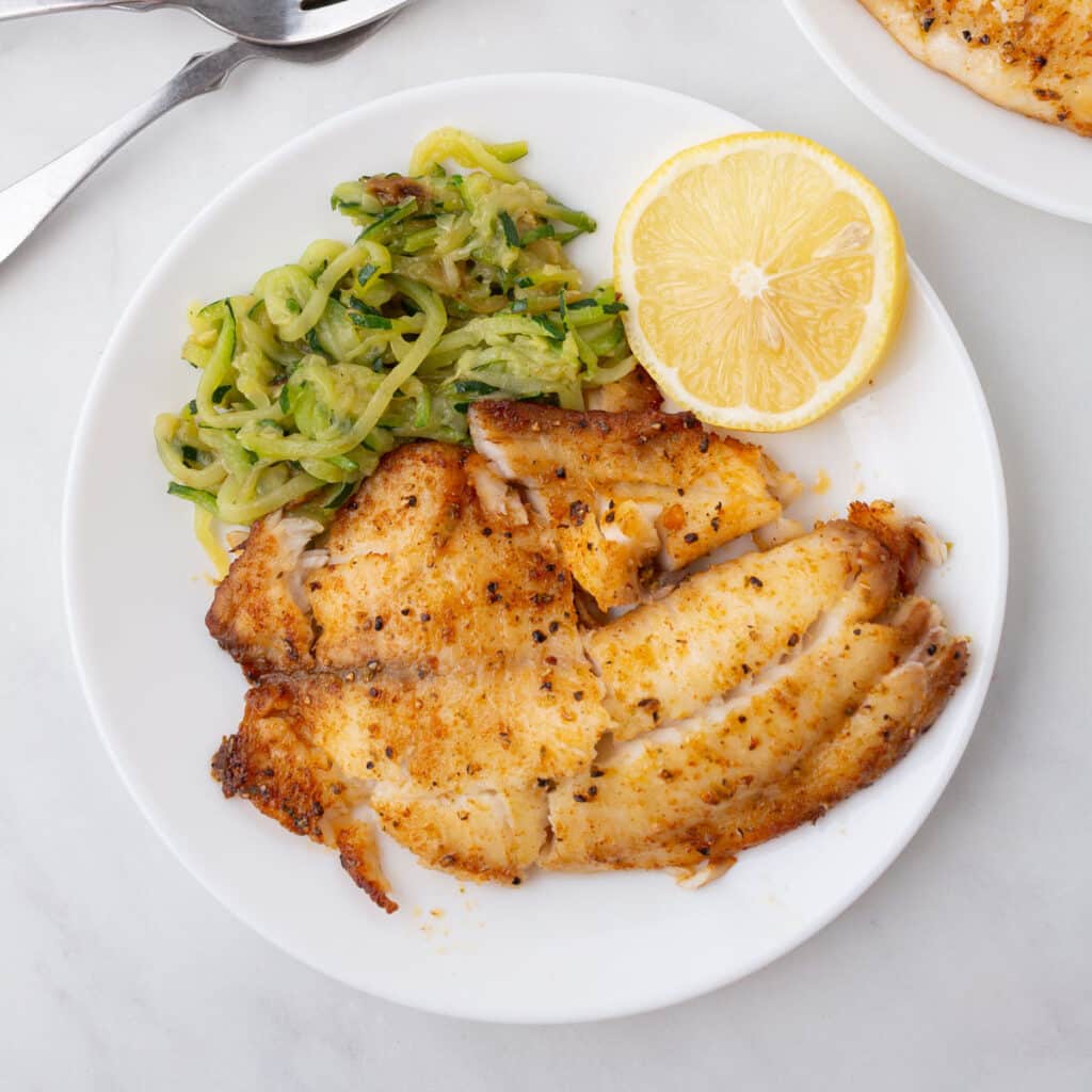 A bird's eye view of a plate with tilapia and some veggies.