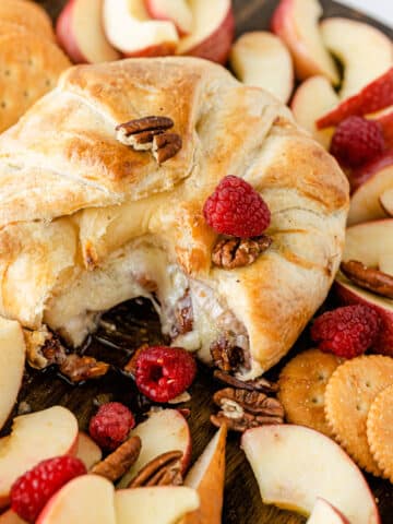 Baked brie with puff pastry with jam and raspberries oozing out of center.