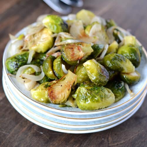 A close up image of roasted Brussels sprouts on a stack of white dishes.