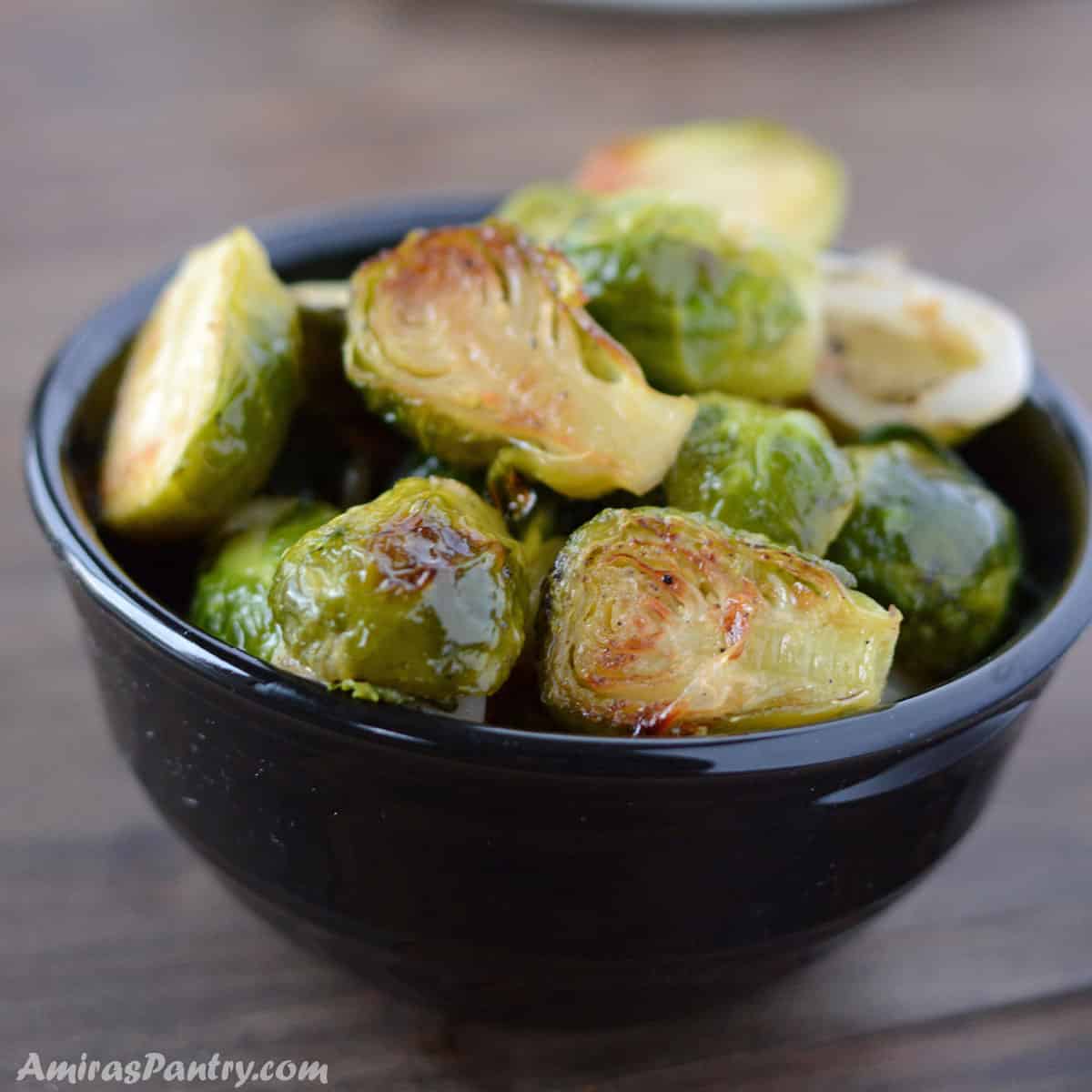 A pile of brussels sprouts in a black bowl placed on a wooden surface.