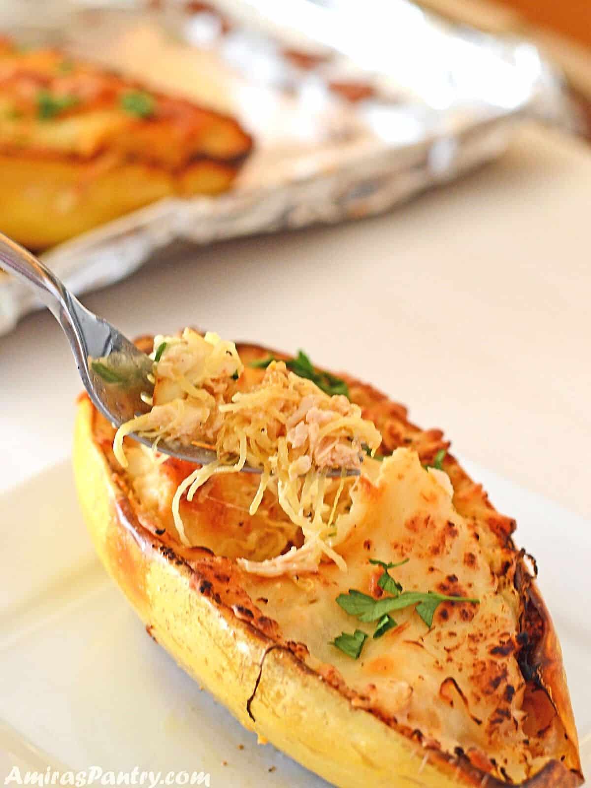 A fork with some chicken spaghetti squash over a spaghetti squash boat garnished with parsley.