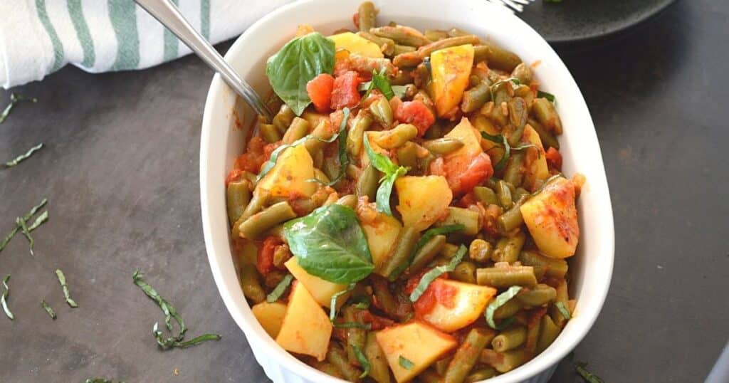 A white casserole with Greek grean beans garnished with fresh basil.