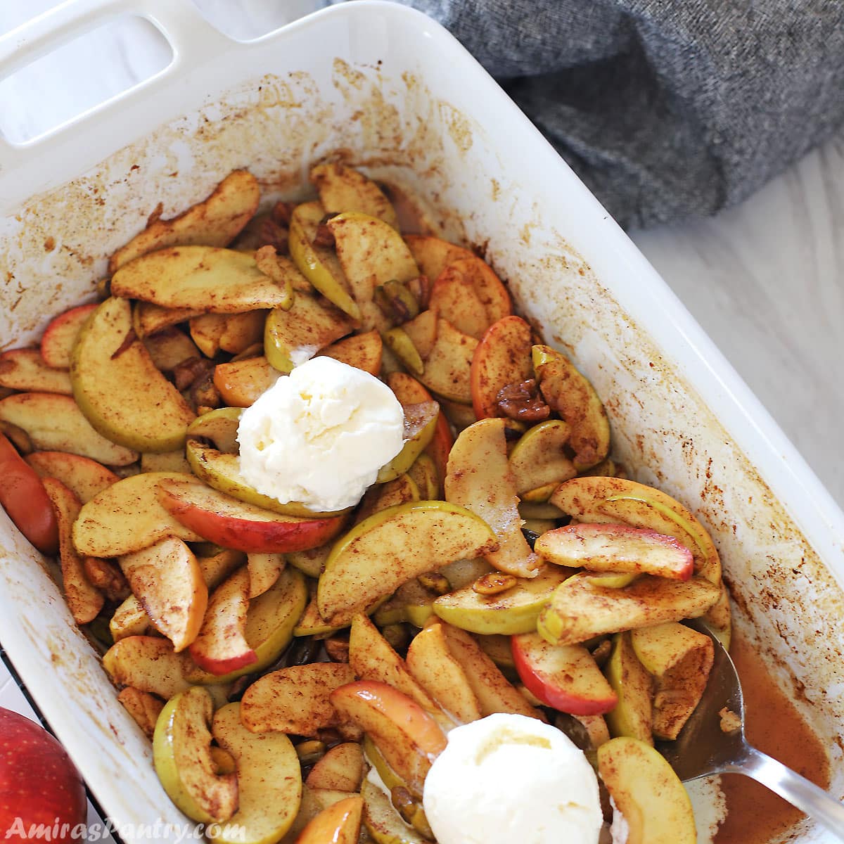 A white oven dish with healthy cinnamon baked apple slices and topped with vanilla ice cream.