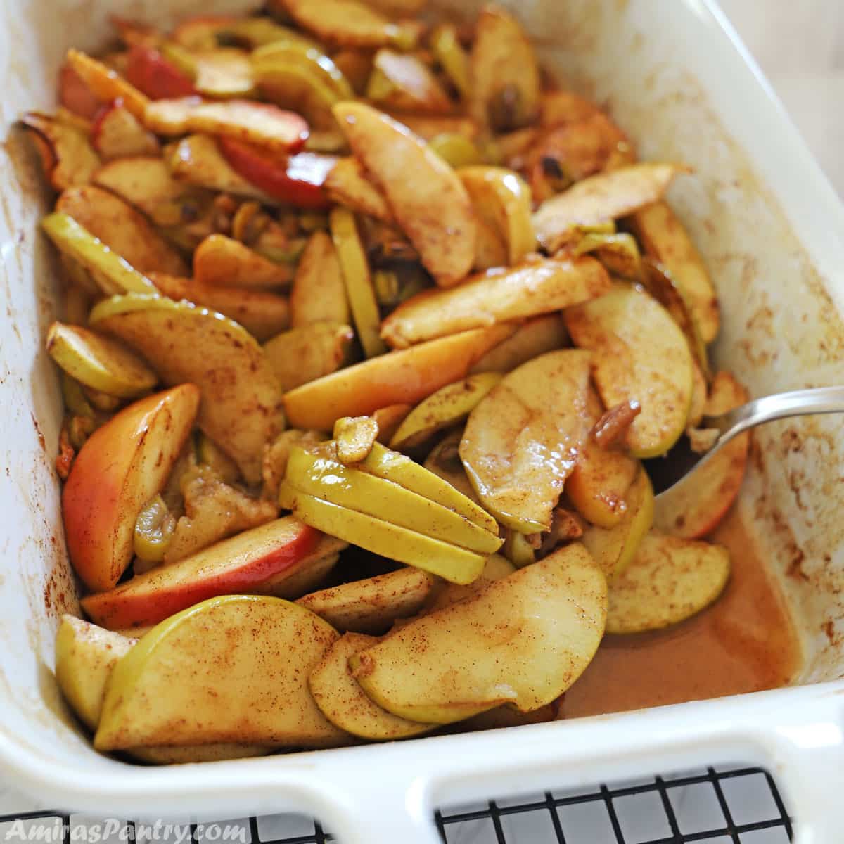 A white ceramic oven dish with healthy baked apple slices with a spoon in it.