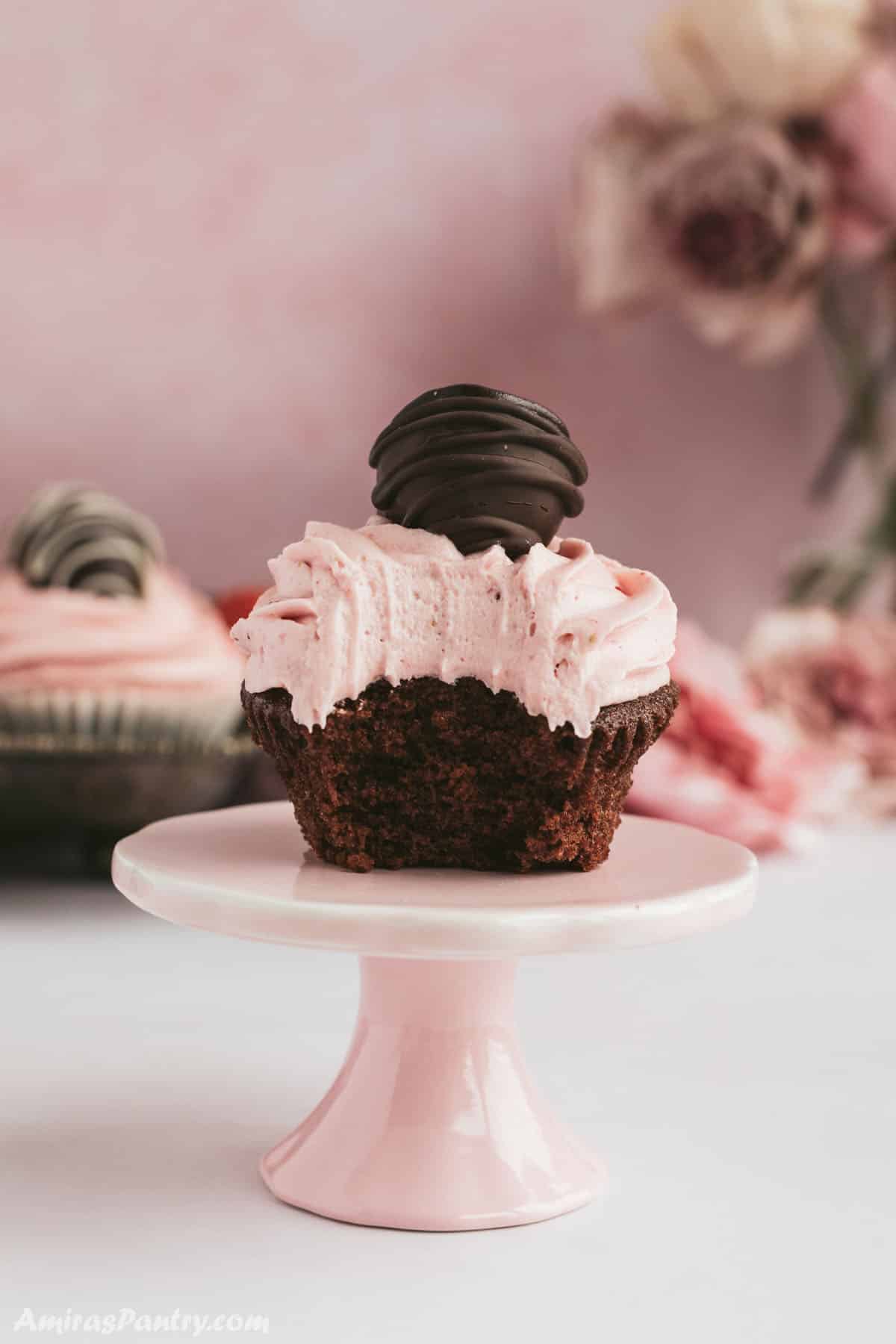 Chocolate cupcake put on a pink stand with a bite taken from it.