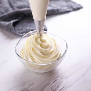 Chantilly cream being piped out in a small glass bowl.