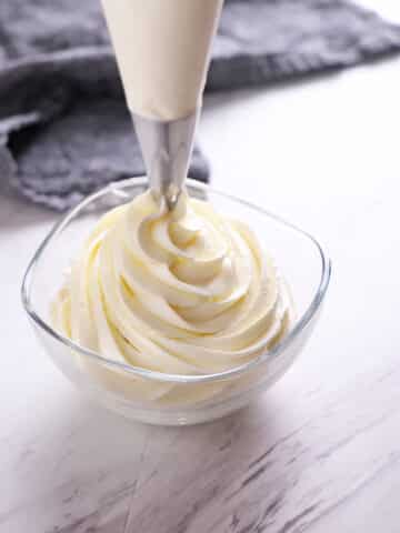 Chantilly cream being piped out in a small glass bowl.