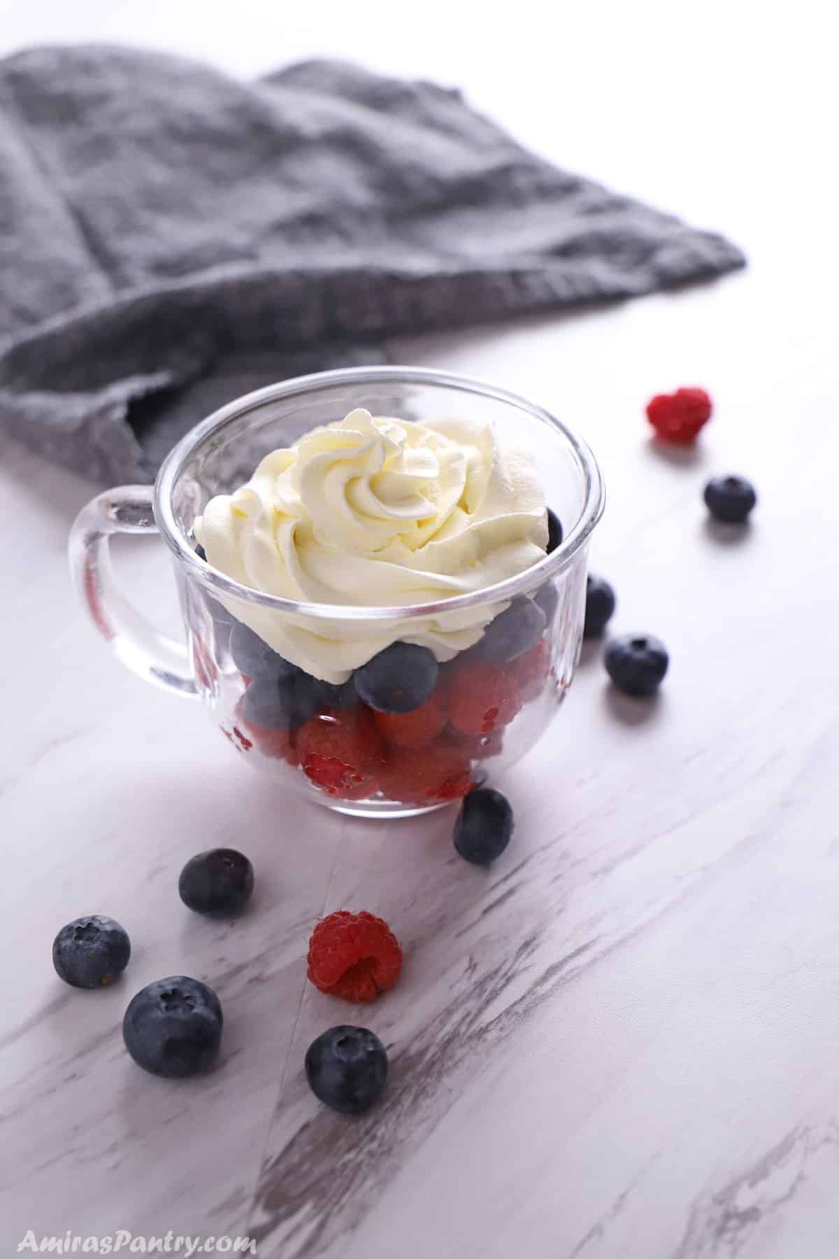 A cup pf berries topped with chantilly cream.