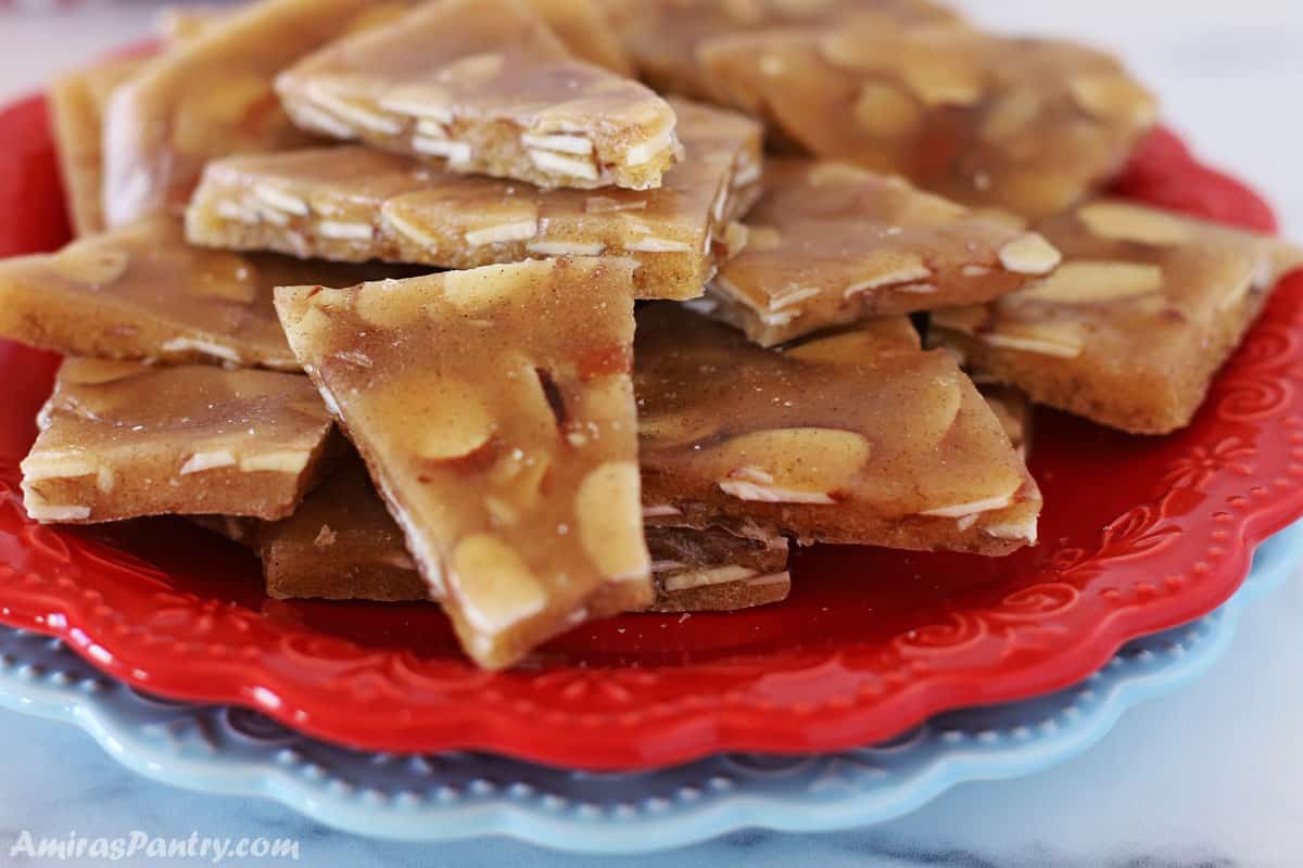 Almond brittle on a red plate with a light blue plate under it.