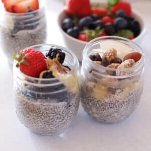 3 jars of chia pudding ona ahite surface garnished with fresh fruits and nuts.