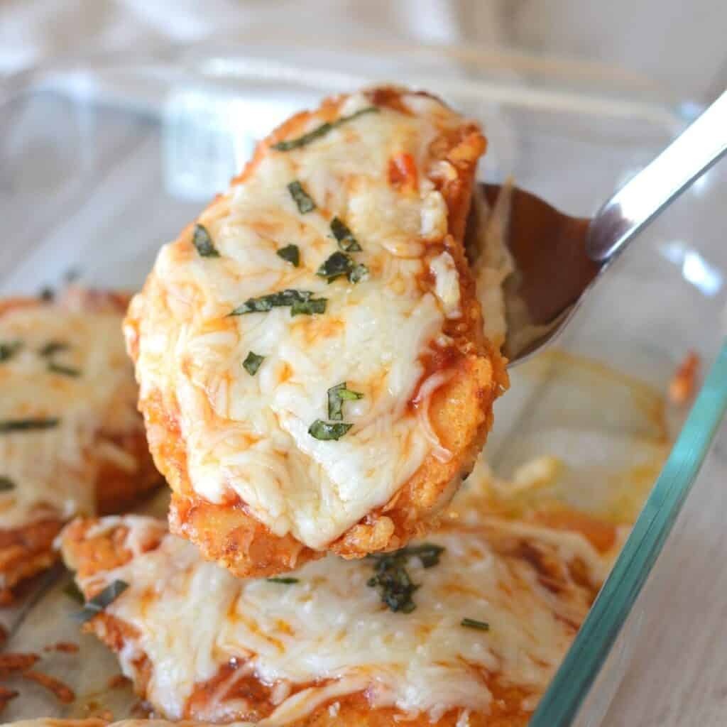 A serving spoon holding a piece of chicken garnished with basil.