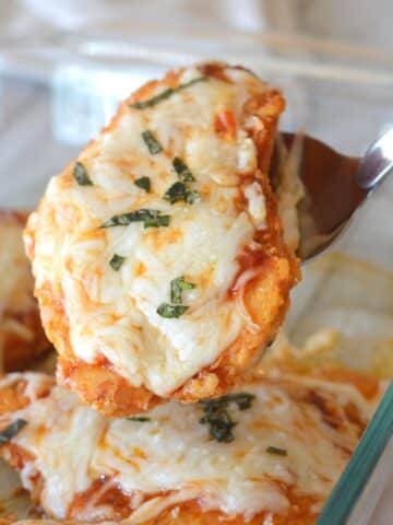 A serving spoon holding a piece of chicken garnished with basil.