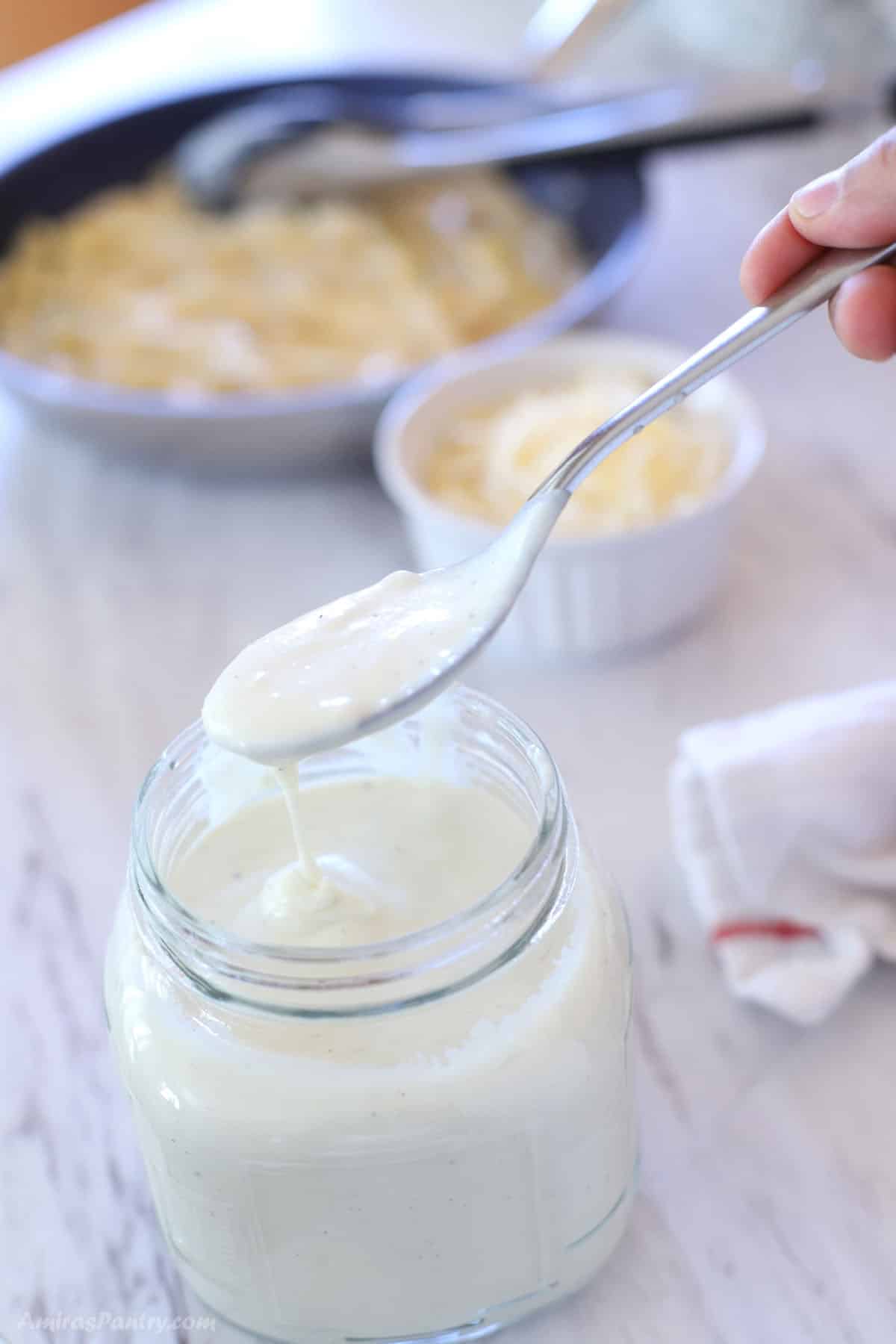 A spoon scooping some alfredo sauce from a jar.