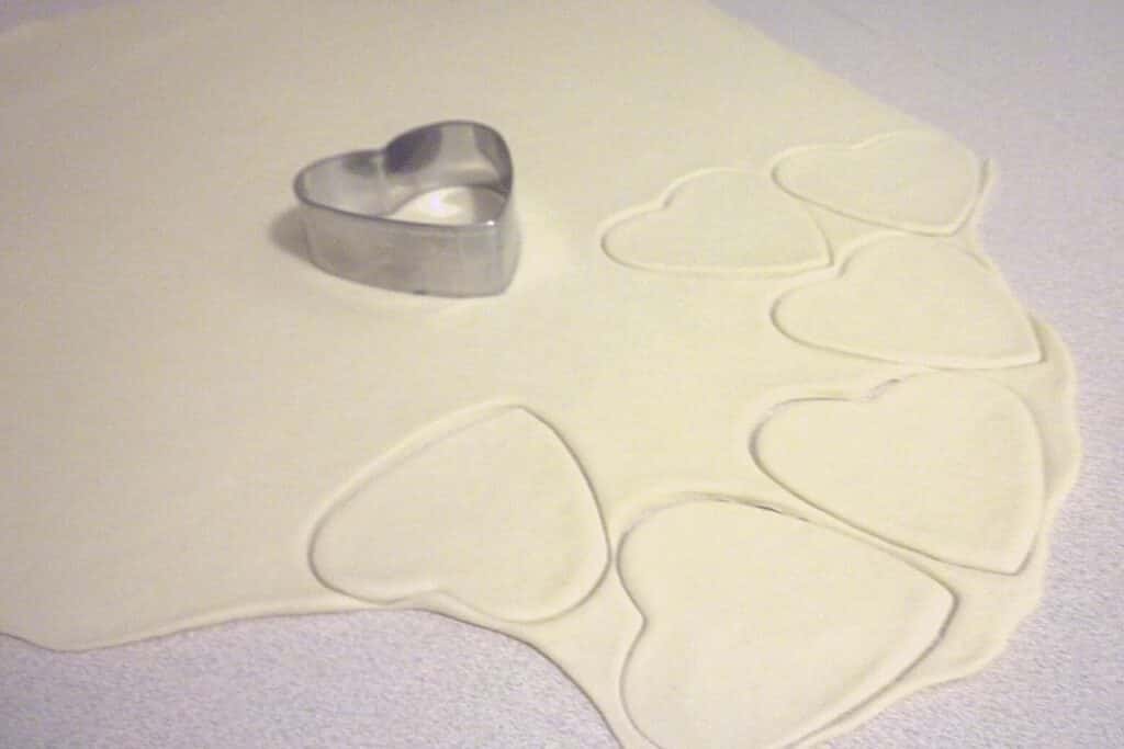 Fritters dough rolled on a countertop and cut with heart shaped cookies.