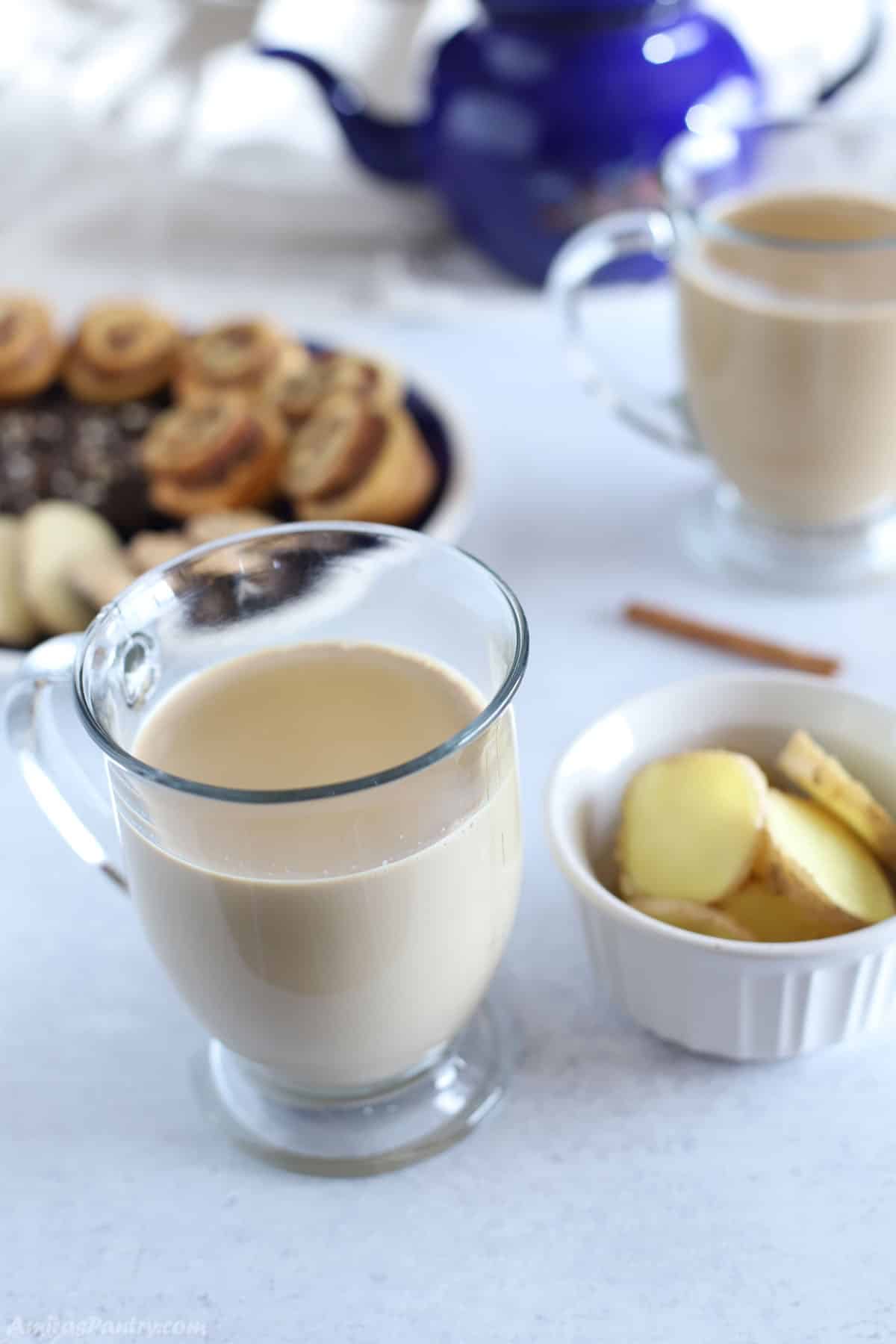 A table with two cups of ginger latte and a plate of cookies on the back.