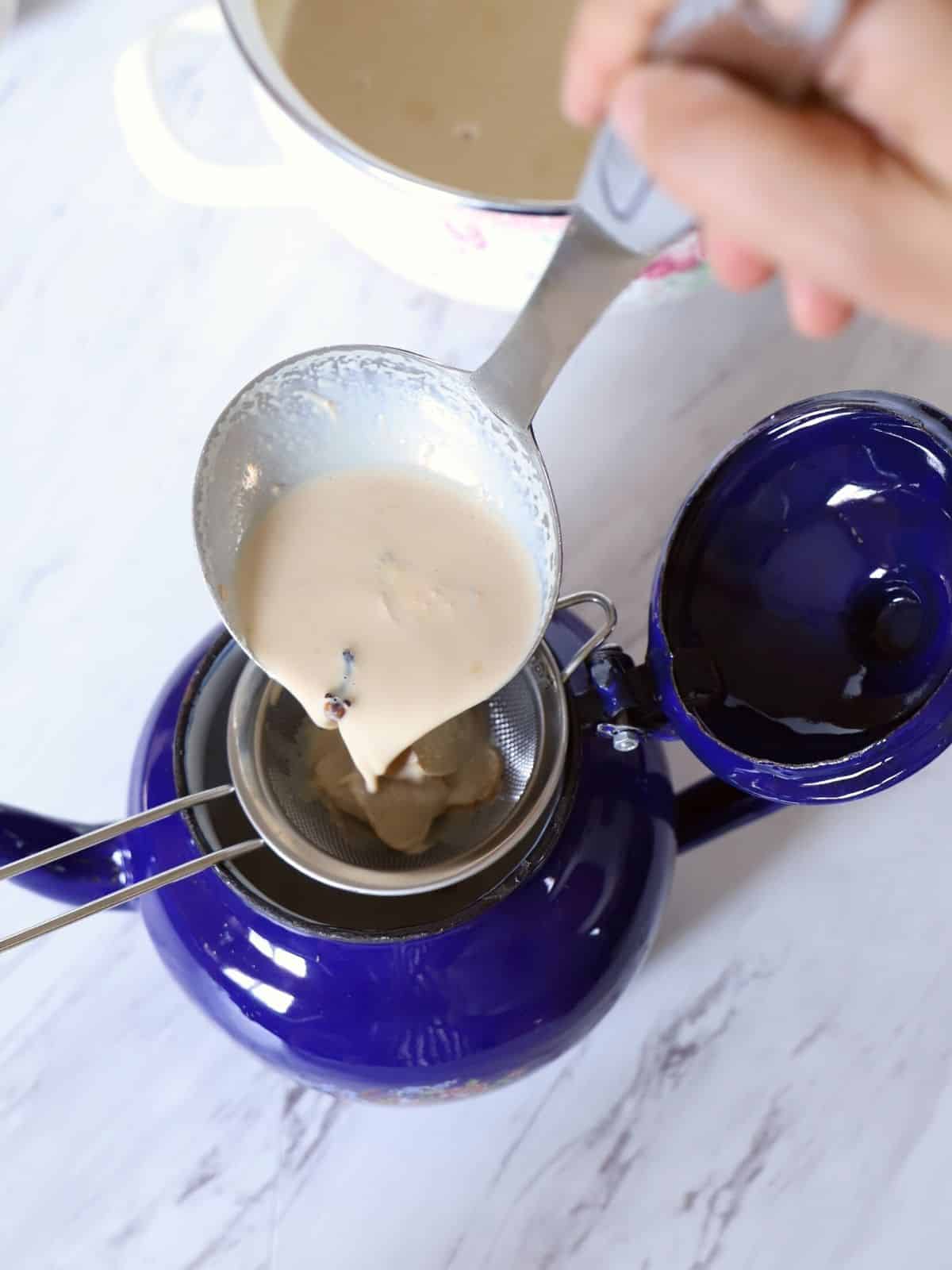 Straining latte into a blue tea pot.