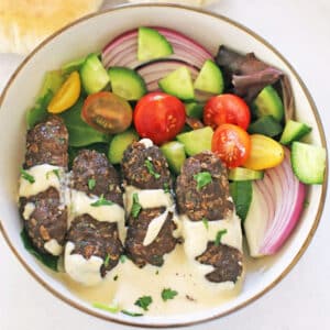 A bird's eye view of a plate with kafta, tahini sauce and green salad.