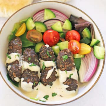 A bird's eye view of a plate with kafta, tahini sauce and green salad.