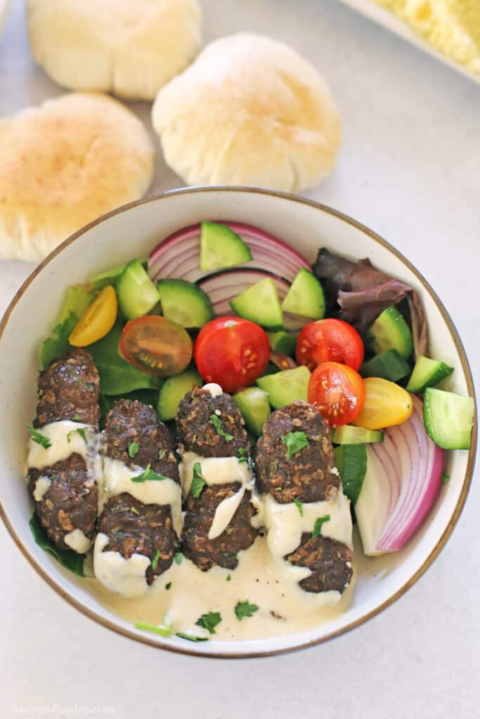 A bird's eye view of a plate with kafta, tahini sauce and green salad.