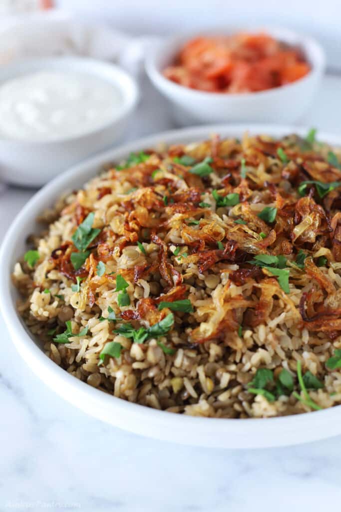 A white serving platter with mujadara garnished with chopped parsley.