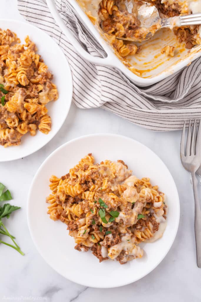 Two white plates with pasta and a baking dish next to them.