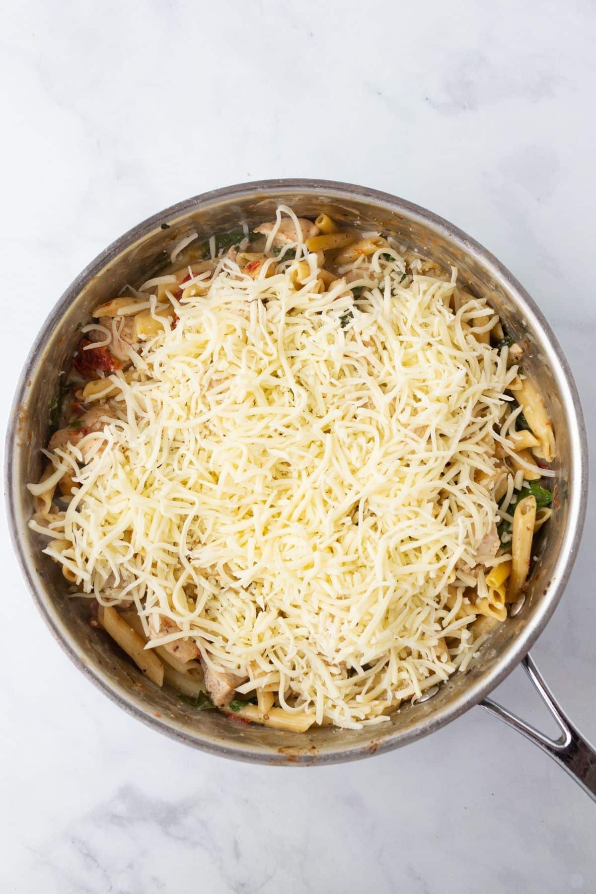 A skillet of tuscan chicken pasta topped with cheese.