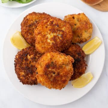 A top view of chicken patties on a white dish with lemon wedges.