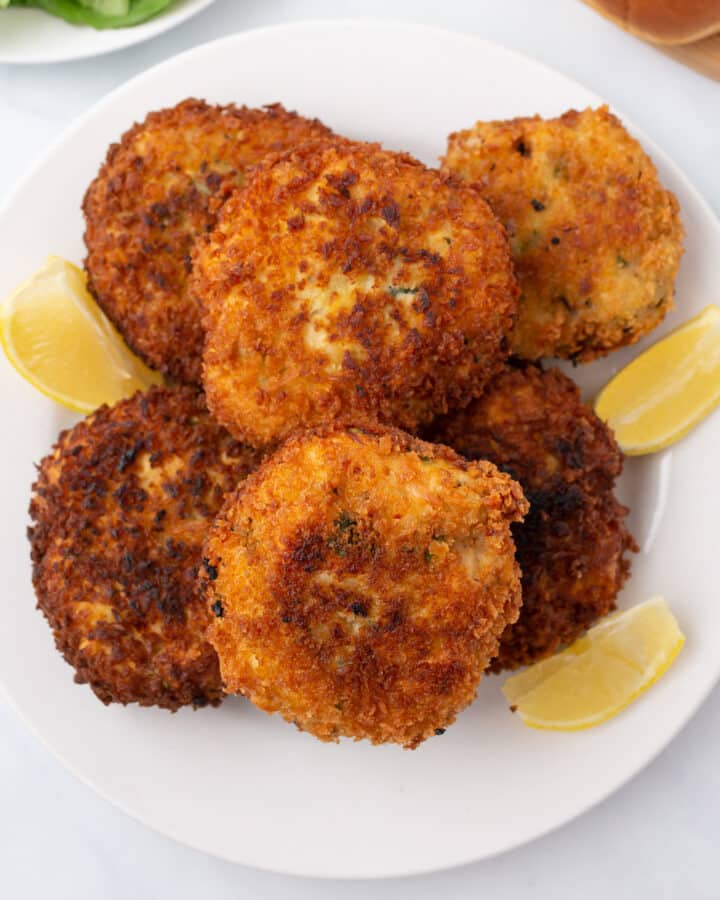 A top view of chicken patties on a white dish with lemon wedges.